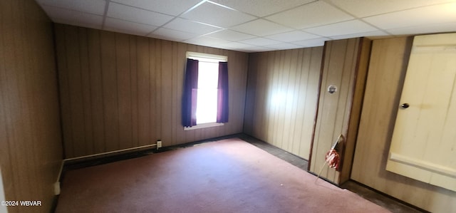 carpeted empty room with a paneled ceiling and wood walls