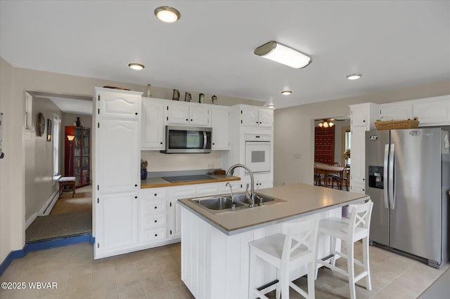 kitchen with appliances with stainless steel finishes, a sink, white cabinetry, a baseboard radiator, and a breakfast bar