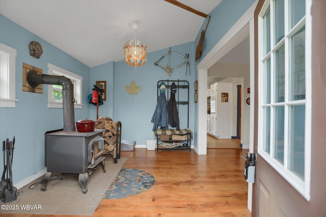 entrance foyer with light wood-style floors, a chandelier, a wood stove, lofted ceiling, and baseboards