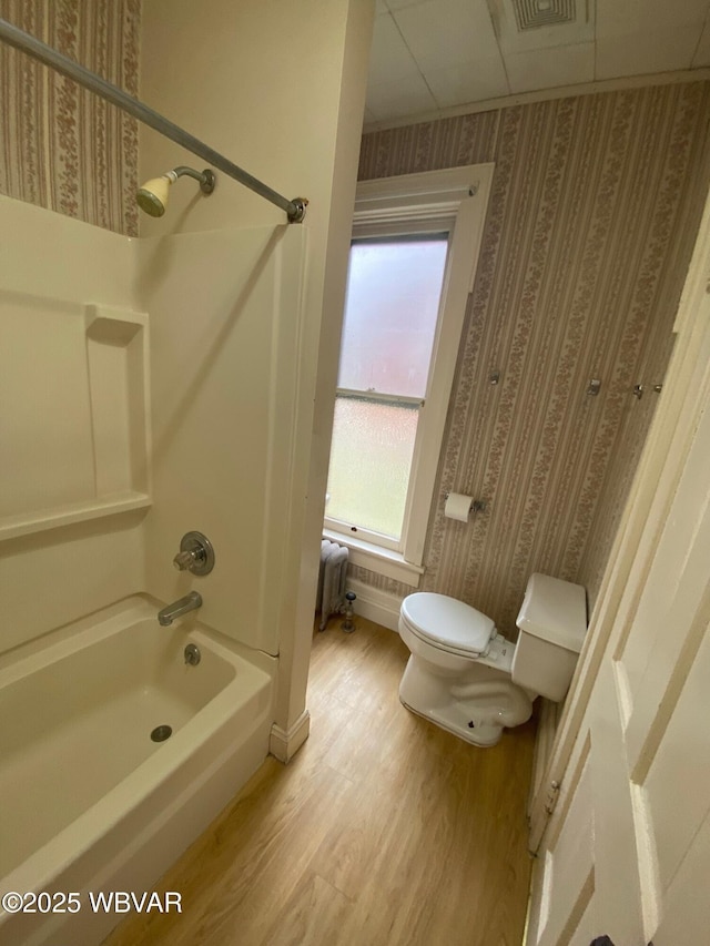 full bath featuring toilet, bathing tub / shower combination, wallpapered walls, radiator heating unit, and wood finished floors