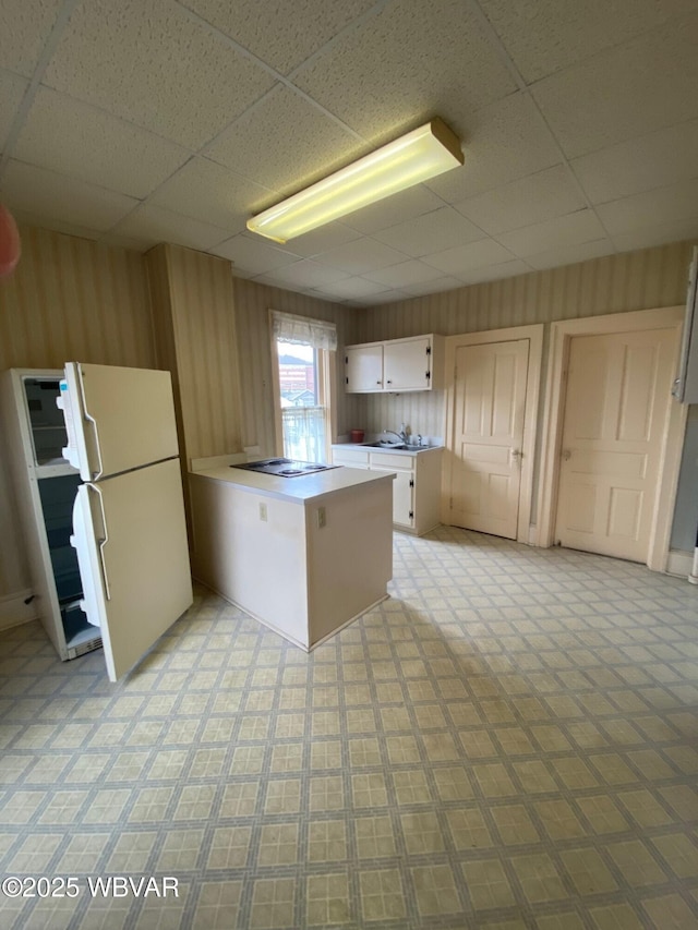kitchen featuring light floors, freestanding refrigerator, white cabinets, a peninsula, and a paneled ceiling