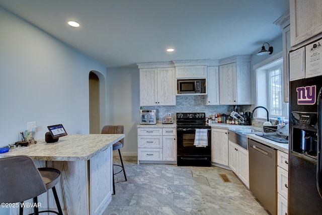 kitchen featuring arched walkways, light countertops, backsplash, black appliances, and a kitchen bar