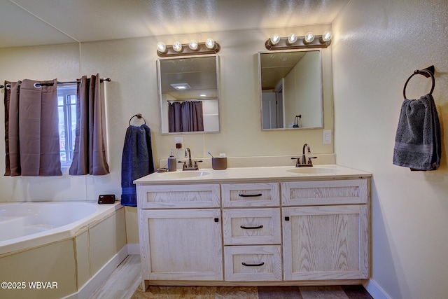 bathroom with a garden tub, double vanity, a sink, and baseboards