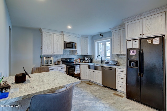 kitchen featuring tasteful backsplash, arched walkways, light countertops, black appliances, and a sink