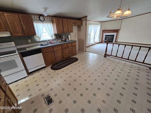 kitchen with pendant lighting, white appliances, sink, a notable chandelier, and a tiled fireplace