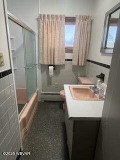 full bathroom featuring tile walls, bath / shower combo with glass door, vanity, a baseboard radiator, and toilet