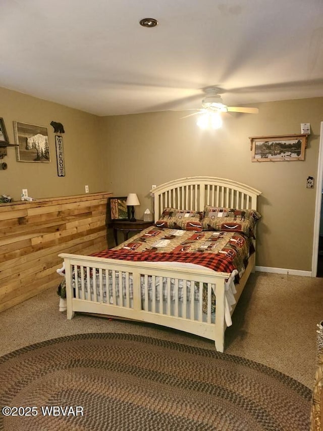 carpeted bedroom featuring ceiling fan and wood walls