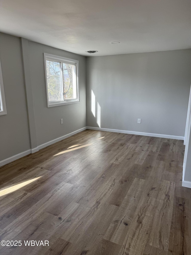 spare room featuring baseboards, visible vents, and wood finished floors