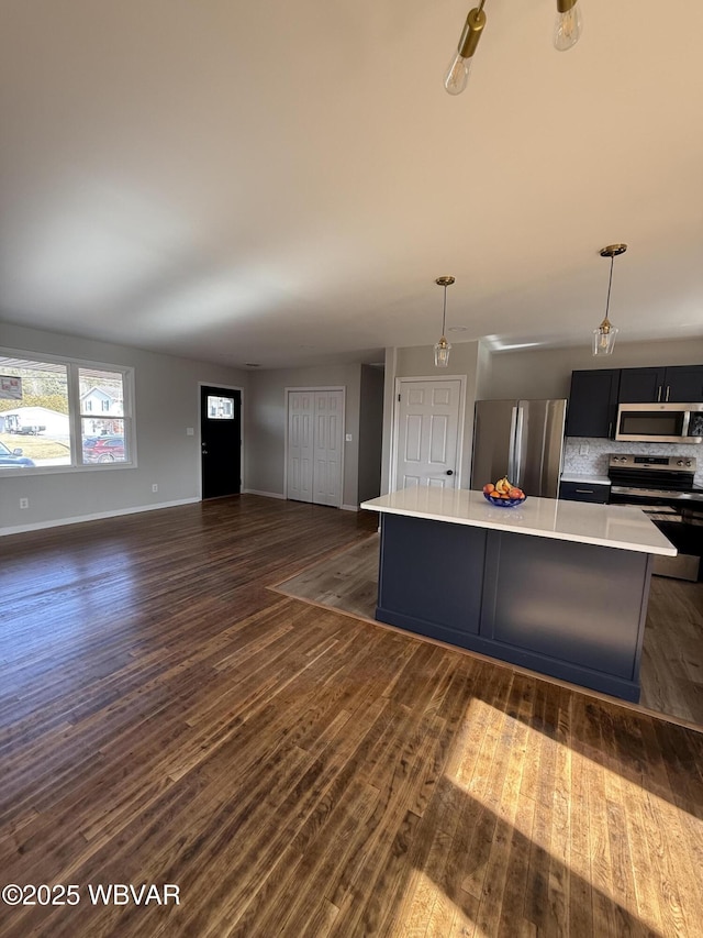 kitchen with dark wood-type flooring, tasteful backsplash, hanging light fixtures, a kitchen island, and stainless steel appliances