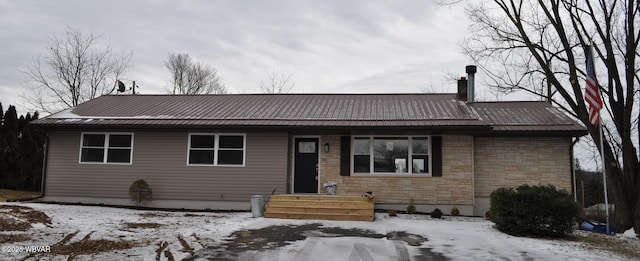 single story home with entry steps, stone siding, metal roof, and a chimney