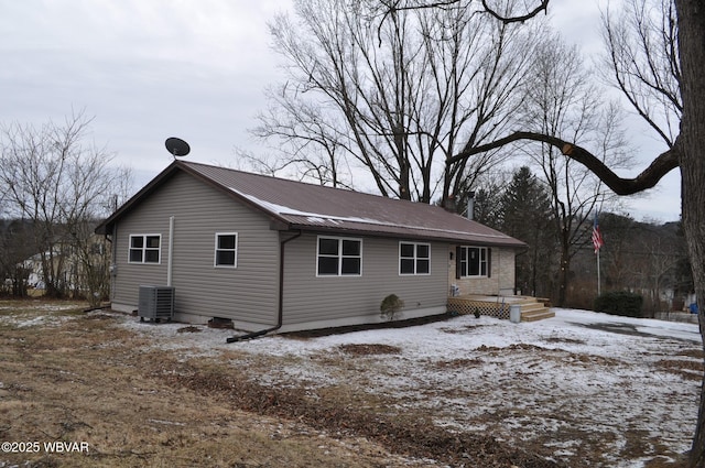 snow covered back of property with central AC unit and metal roof