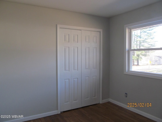 unfurnished bedroom with dark wood-style floors, baseboards, and a closet