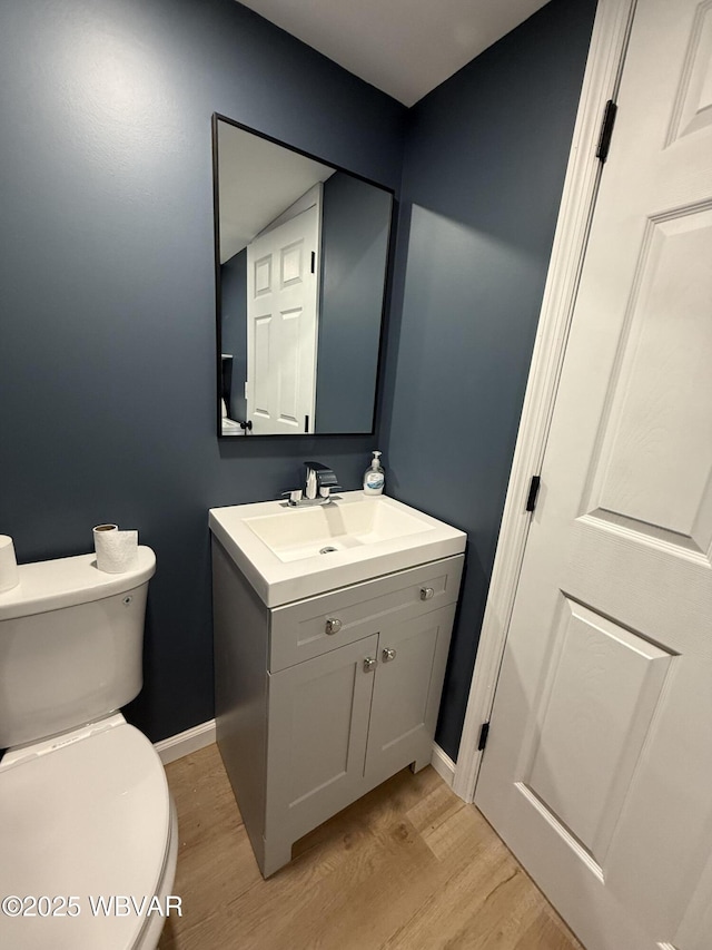 half bath featuring toilet, baseboards, wood finished floors, and vanity