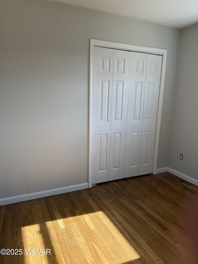 unfurnished bedroom featuring baseboards, dark wood finished floors, and a closet