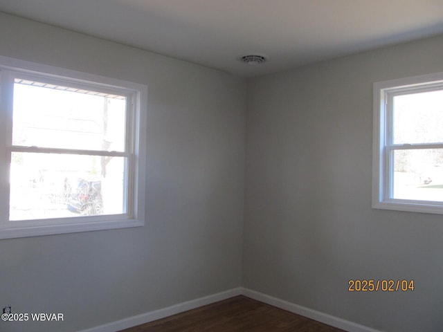 empty room featuring dark wood-type flooring, visible vents, and baseboards