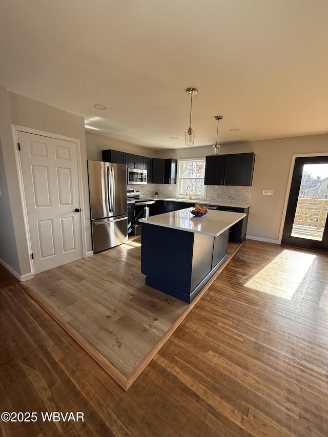 kitchen featuring a kitchen island, appliances with stainless steel finishes, tasteful backsplash, dark hardwood / wood-style flooring, and hanging light fixtures