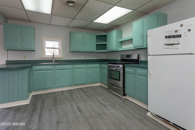 kitchen featuring sink, white refrigerator, stainless steel gas range, light hardwood / wood-style floors, and a drop ceiling