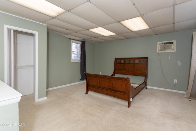 bedroom with light colored carpet, a drop ceiling, and a wall unit AC