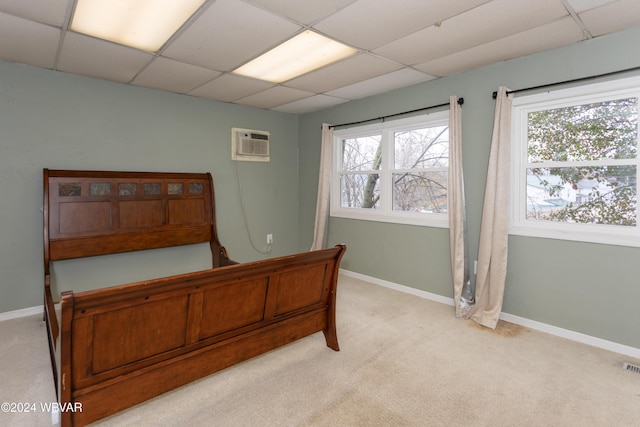 bedroom with a paneled ceiling, a wall mounted air conditioner, and light carpet