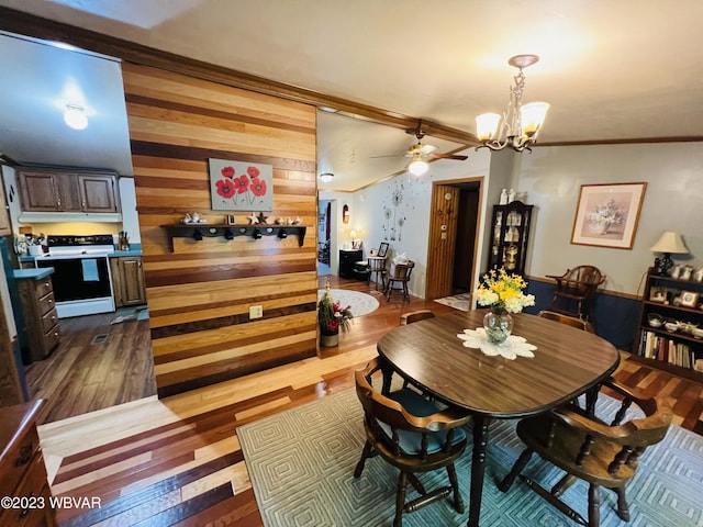 dining space with wooden walls, ceiling fan with notable chandelier, dark hardwood / wood-style floors, and crown molding