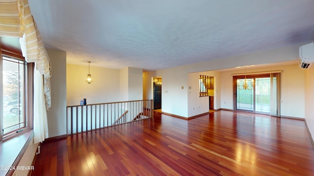 unfurnished room with hardwood / wood-style floors, an AC wall unit, and a notable chandelier