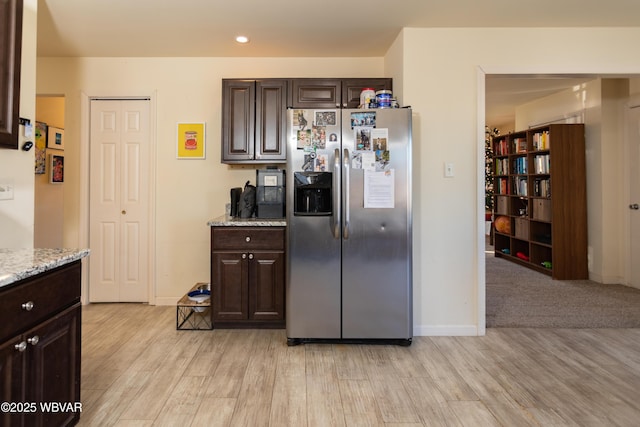 kitchen with dark brown cabinetry, stainless steel fridge with ice dispenser, light hardwood / wood-style floors, and light stone counters