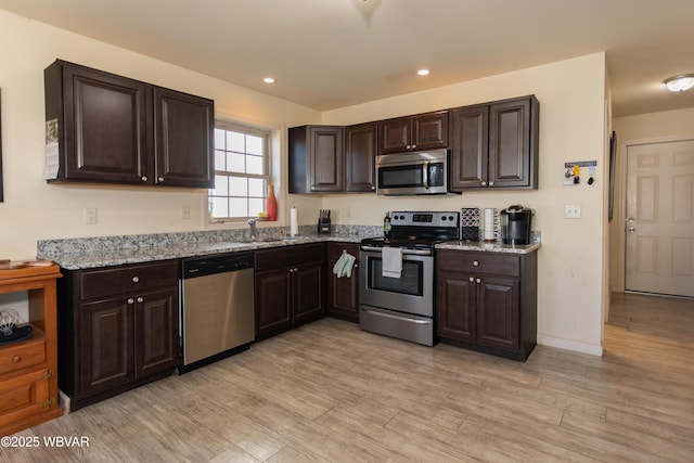 kitchen with sink, light stone counters, dark brown cabinets, appliances with stainless steel finishes, and light wood-type flooring