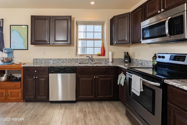 kitchen featuring appliances with stainless steel finishes, light stone counters, dark brown cabinets, sink, and light hardwood / wood-style floors