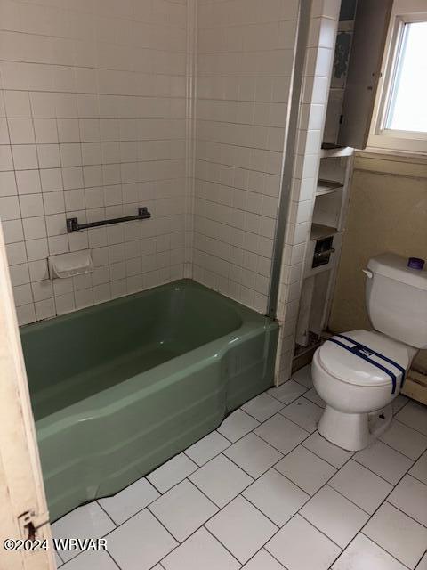 bathroom featuring tile patterned flooring, toilet, and tiled shower / bath