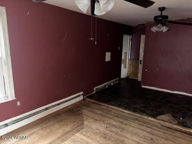 empty room featuring hardwood / wood-style flooring, ceiling fan, and a baseboard radiator