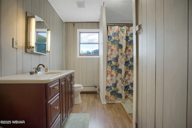 bathroom with hardwood / wood-style floors, wood walls, vanity, a baseboard heating unit, and toilet