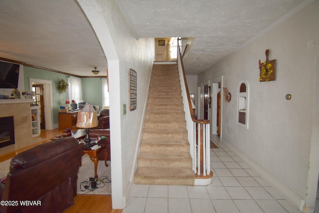 45 W Bald Eagle St, Lock Haven, PA 17745 - staircase featuring a textured ceiling, arched walkways, a glass covered fireplace, ornamental molding, and tile patterned floors