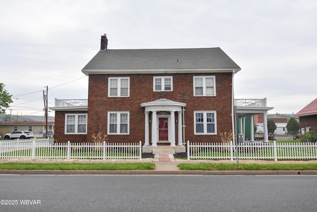 colonial home featuring a chimney, a fenced front yard, and brick siding