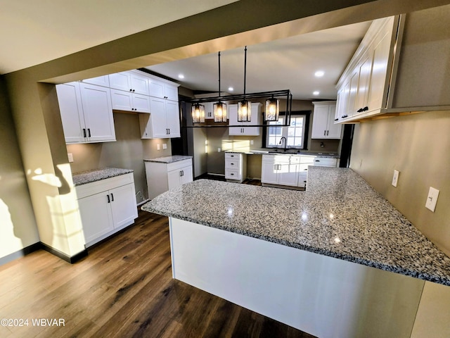 kitchen with pendant lighting, dark wood-type flooring, sink, dark stone countertops, and white cabinetry