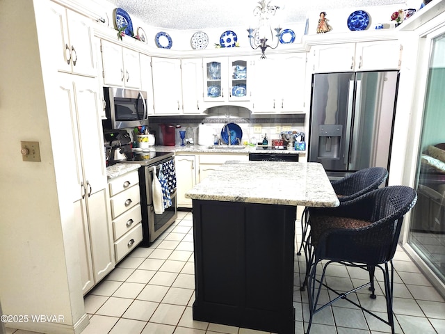 kitchen featuring stainless steel appliances, light tile patterned floors, a center island, and white cabinets