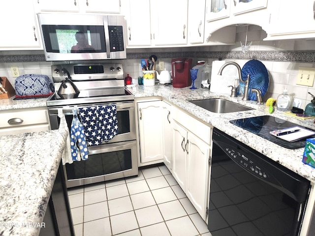 kitchen with appliances with stainless steel finishes, a sink, white cabinets, light tile patterned flooring, and tasteful backsplash