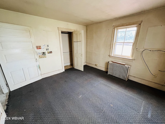 unfurnished bedroom featuring dark colored carpet and radiator heating unit