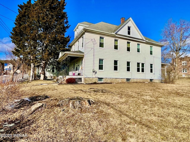 rear view of house with covered porch, a chimney, fence, and a lawn