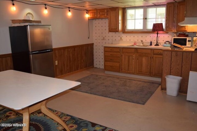 kitchen with stainless steel fridge, a drop ceiling, wooden walls, and sink