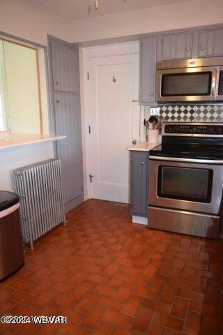 kitchen featuring decorative backsplash, radiator heating unit, stainless steel appliances, and gray cabinets