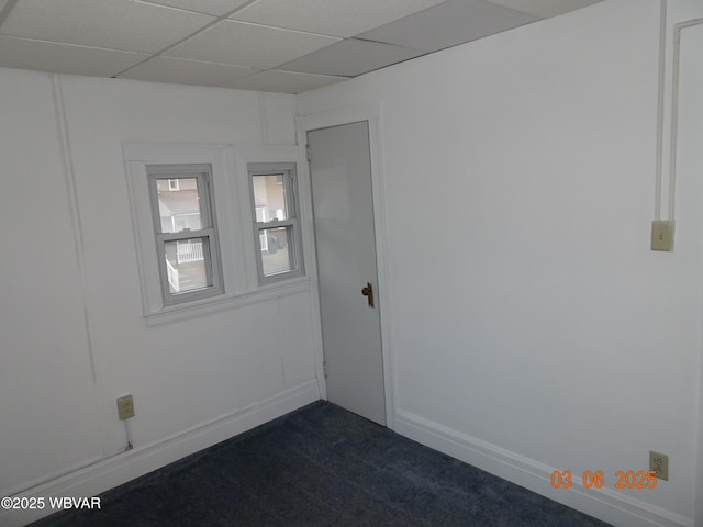 unfurnished room with dark colored carpet, a paneled ceiling, and baseboards