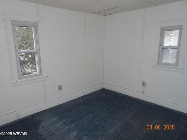 empty room featuring dark carpet, a decorative wall, and a drop ceiling