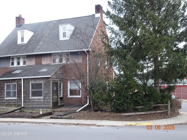 view of front of house with a shingled roof, a chimney, and brick siding