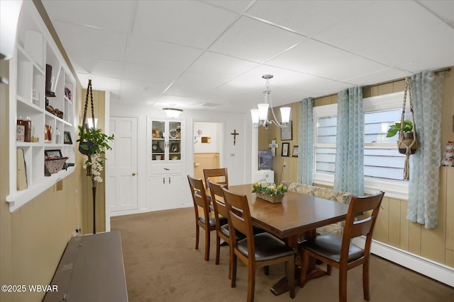 carpeted dining area with a drop ceiling, a notable chandelier, and baseboard heating