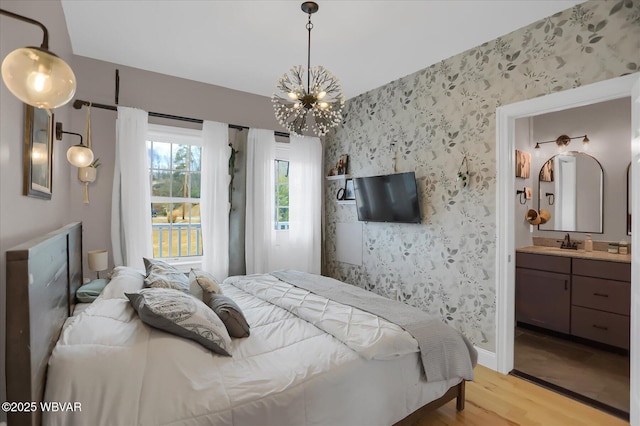 bedroom featuring sink, ensuite bathroom, a chandelier, and light hardwood / wood-style flooring