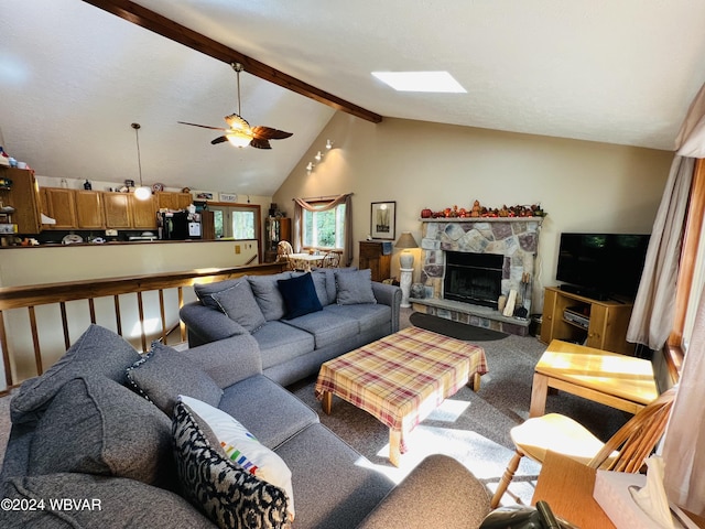 living room with vaulted ceiling with skylight, ceiling fan, and a stone fireplace