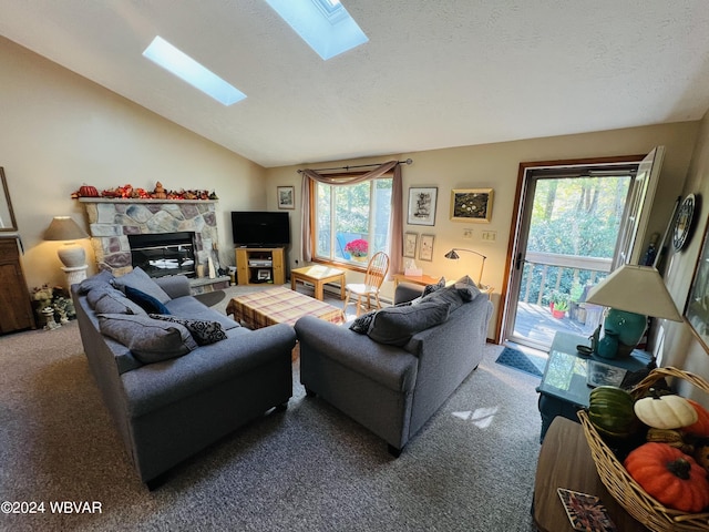 living room with carpet floors, a stone fireplace, a wealth of natural light, and vaulted ceiling with skylight