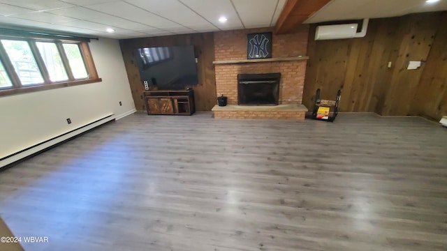 unfurnished living room featuring hardwood / wood-style flooring, wood walls, a brick fireplace, and an AC wall unit