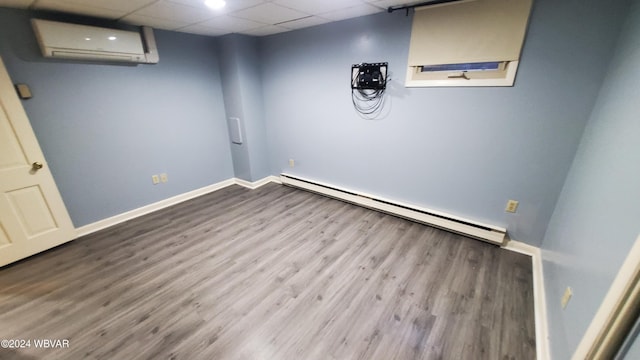 basement with a drop ceiling, wood-type flooring, a wall mounted AC, and baseboard heating