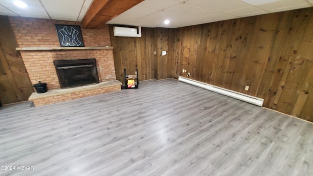 unfurnished living room with wooden walls, a fireplace, wood-type flooring, a wall mounted AC, and a baseboard heating unit